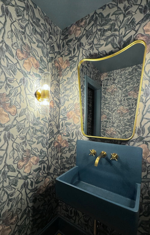 Floral-inspired wallpaper paired with gold-framed mirror and blue fixtures in a modern powder room