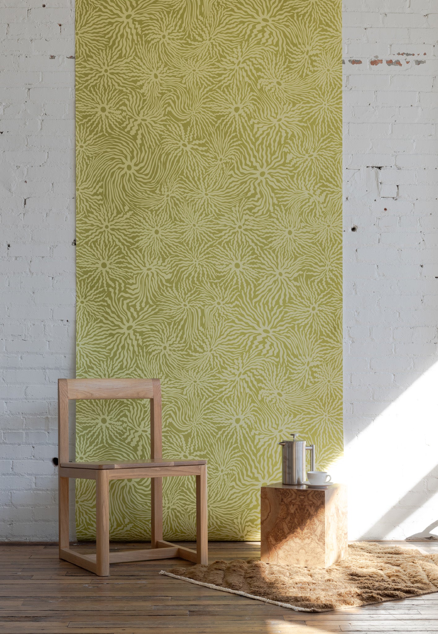 Minimalist room with light wooden chair, small square table, and stainless steel
coffee pot, set against green patterned wallpaper with swirling floral sun design.