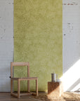 Minimalist room with light wooden chair, small square table, and stainless steel
coffee pot, set against green patterned wallpaper with swirling floral sun design.