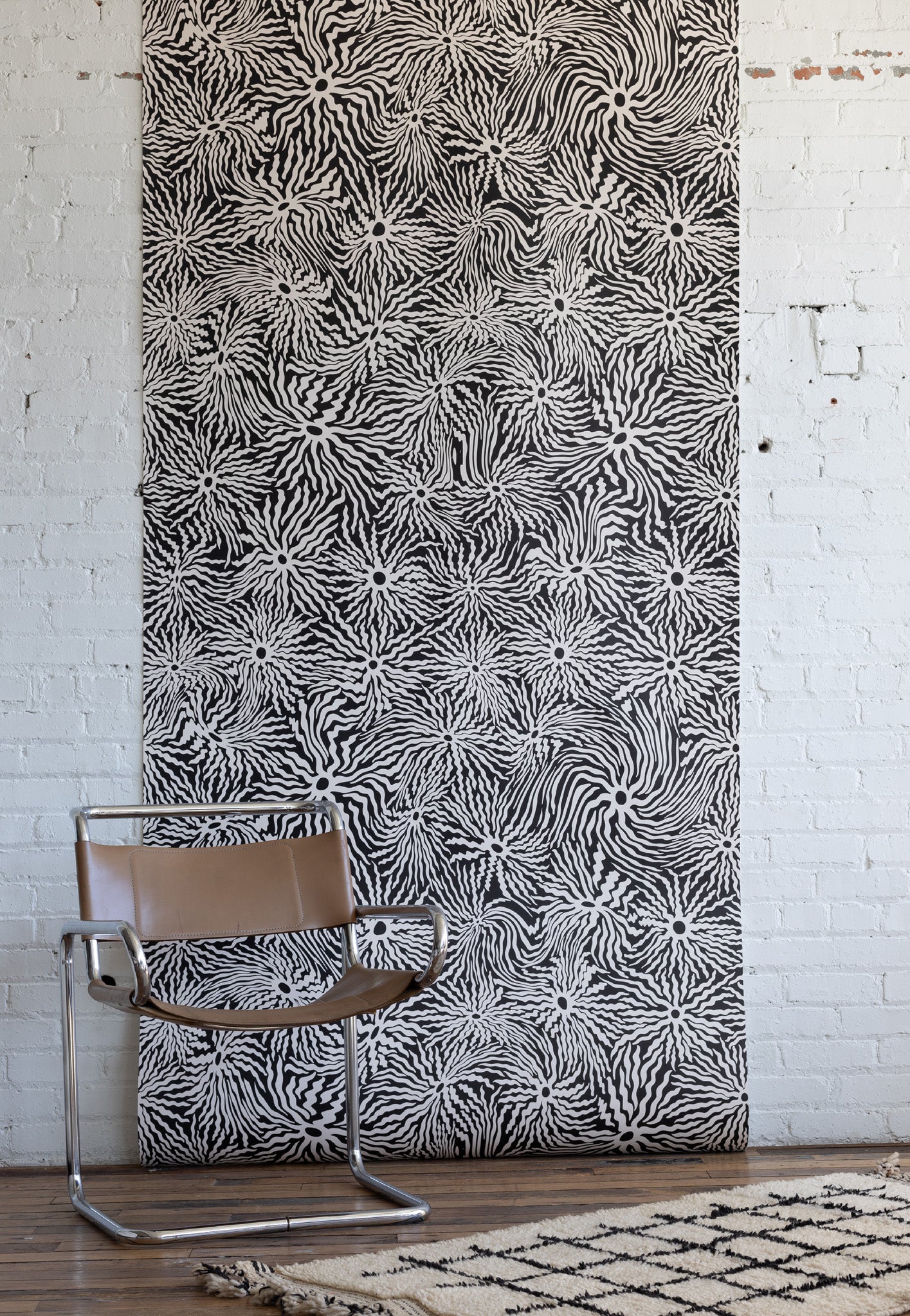 Modern interior featuring brown leather and chrome chair, black and white
patterned wallpaper with abstract swirl design, and light wooden flooring.