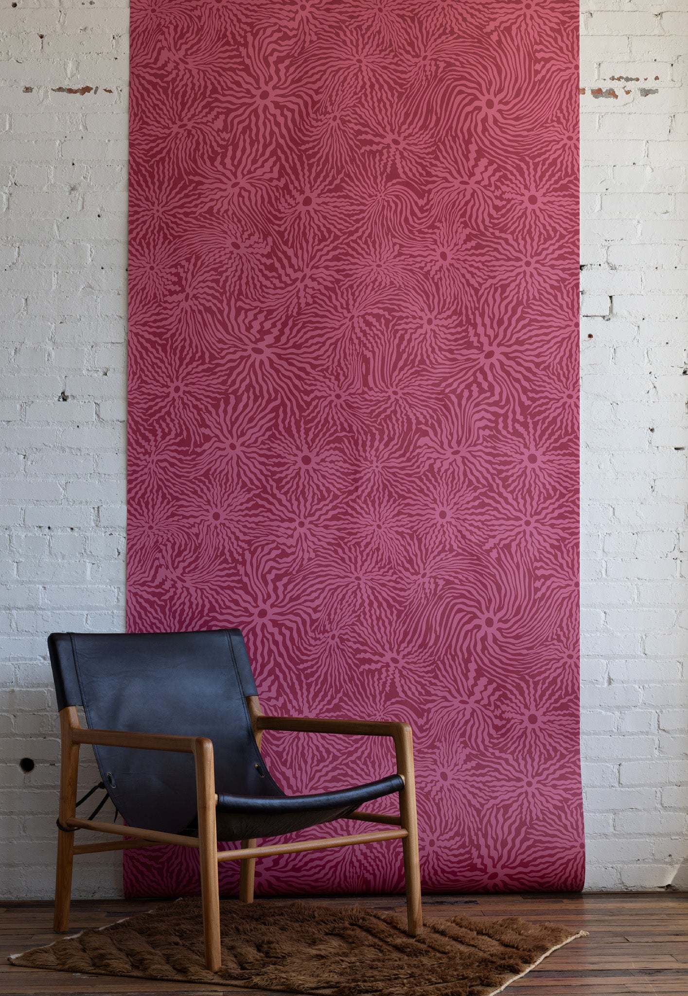 Contemporary black leather armchair with wooden frame placed in front of pink
patterned wallpaper with swirling abstract design on a textured rug.