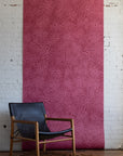 Contemporary black leather armchair with wooden frame placed in front of pink
patterned wallpaper with swirling abstract design on a textured rug.