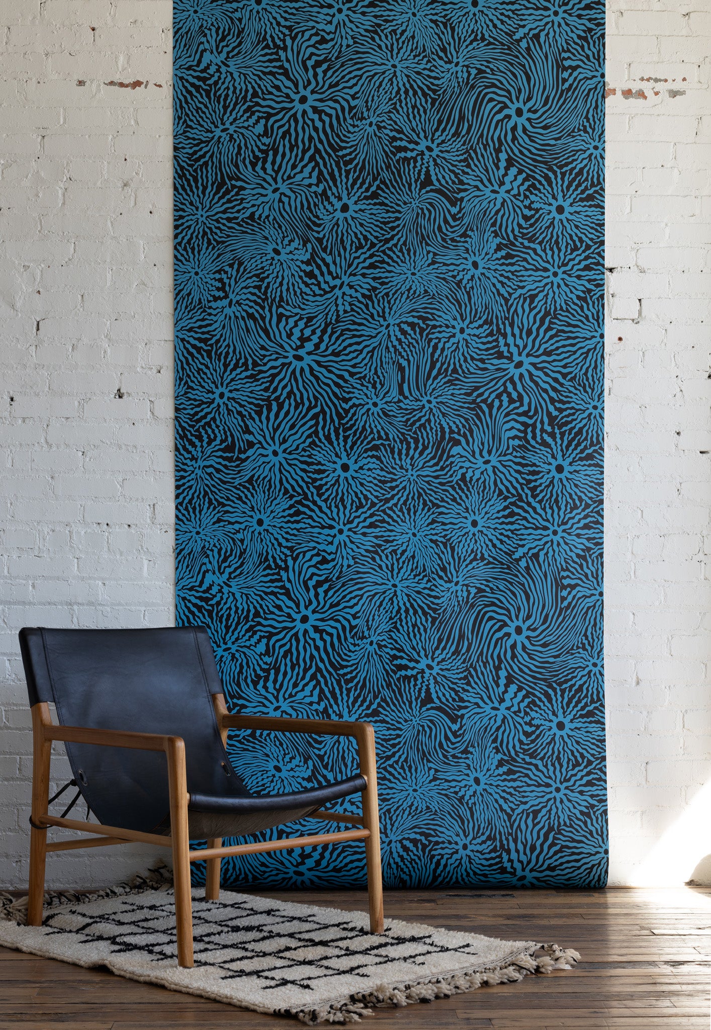 Modern room with black leather armchair, wooden frame, and blue patterned
wallpaper with swirling floral design on a dark background, set on a textured white
rug.