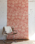 Stylish tan leather and chrome chair draped with a white blanket, placed in front of
red patterned wallpaper with abstract swirling design, on a fluffy cream rug.