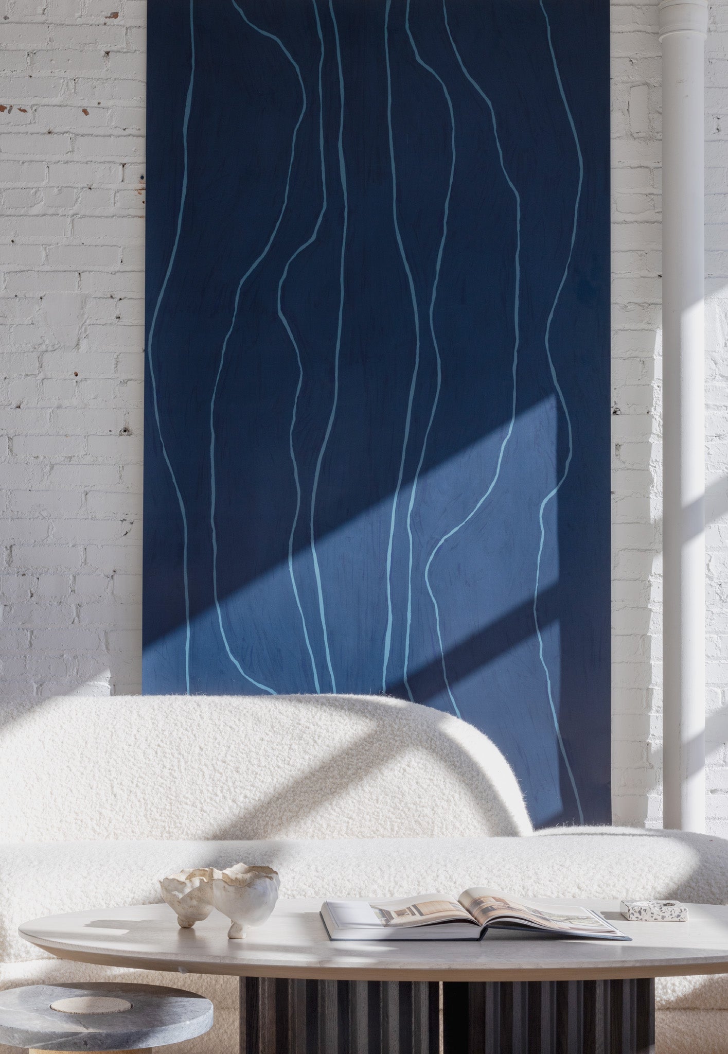 Deep navy-blue wallpaper with light blue vertical wavy lines, behind a boucle sofa and a modern coffee table featuring ceramics and an open book.