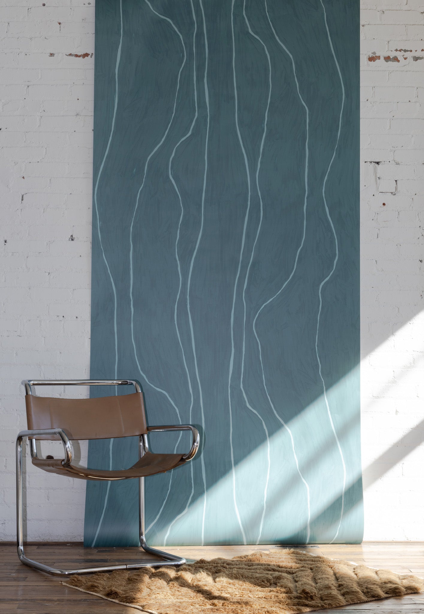 Dark teal wallpaper with subtle wavy vertical lines in light blue, styled with a modern leather and chrome chair on a textured beige rug.