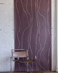 Plum-colored wallpaper with soft pink vertical organic lines, styled with a leather and chrome chair and a deep brown textured rug.