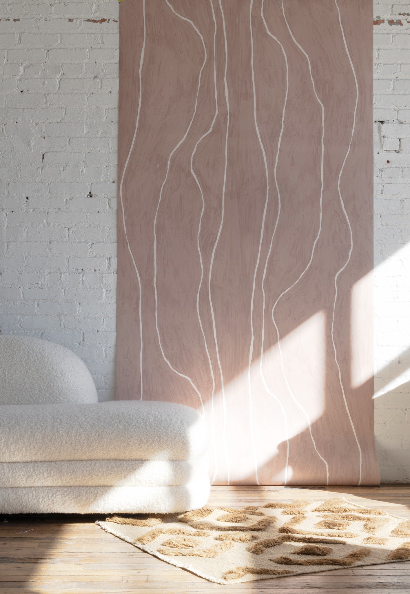 Warm blush wallpaper with organic white vertical lines, styled with a boucle sofa and a beige geometric-pattern rug on a wooden floor.