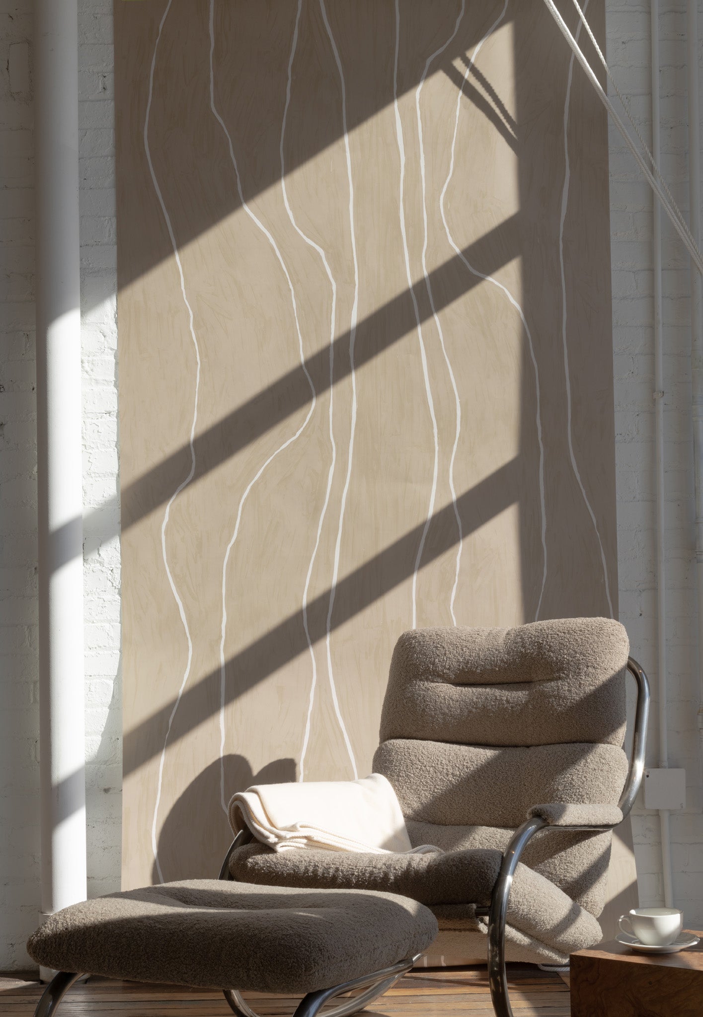 Light taupe wallpaper with white vertical organic lines, styled with a mid-century modern lounge chair and ottoman in soft boucle fabric.